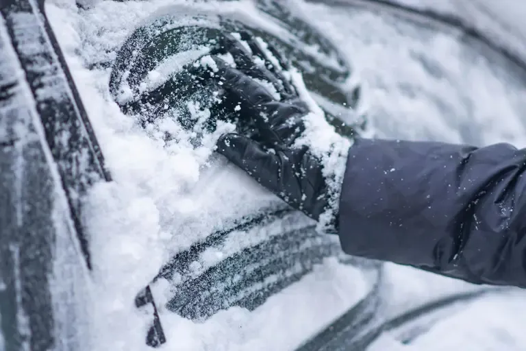 Gloved hand brushing snow off a car windshield in winter