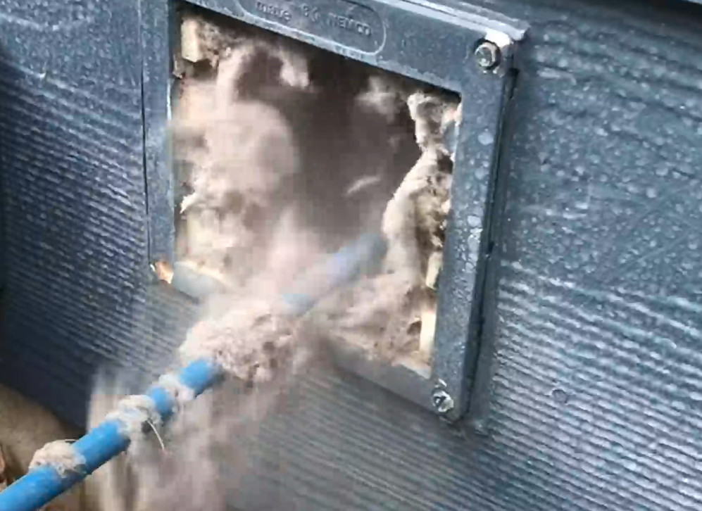 Dryer vent being cleaned with compressed-air whip, dislodging heavy lint buildup